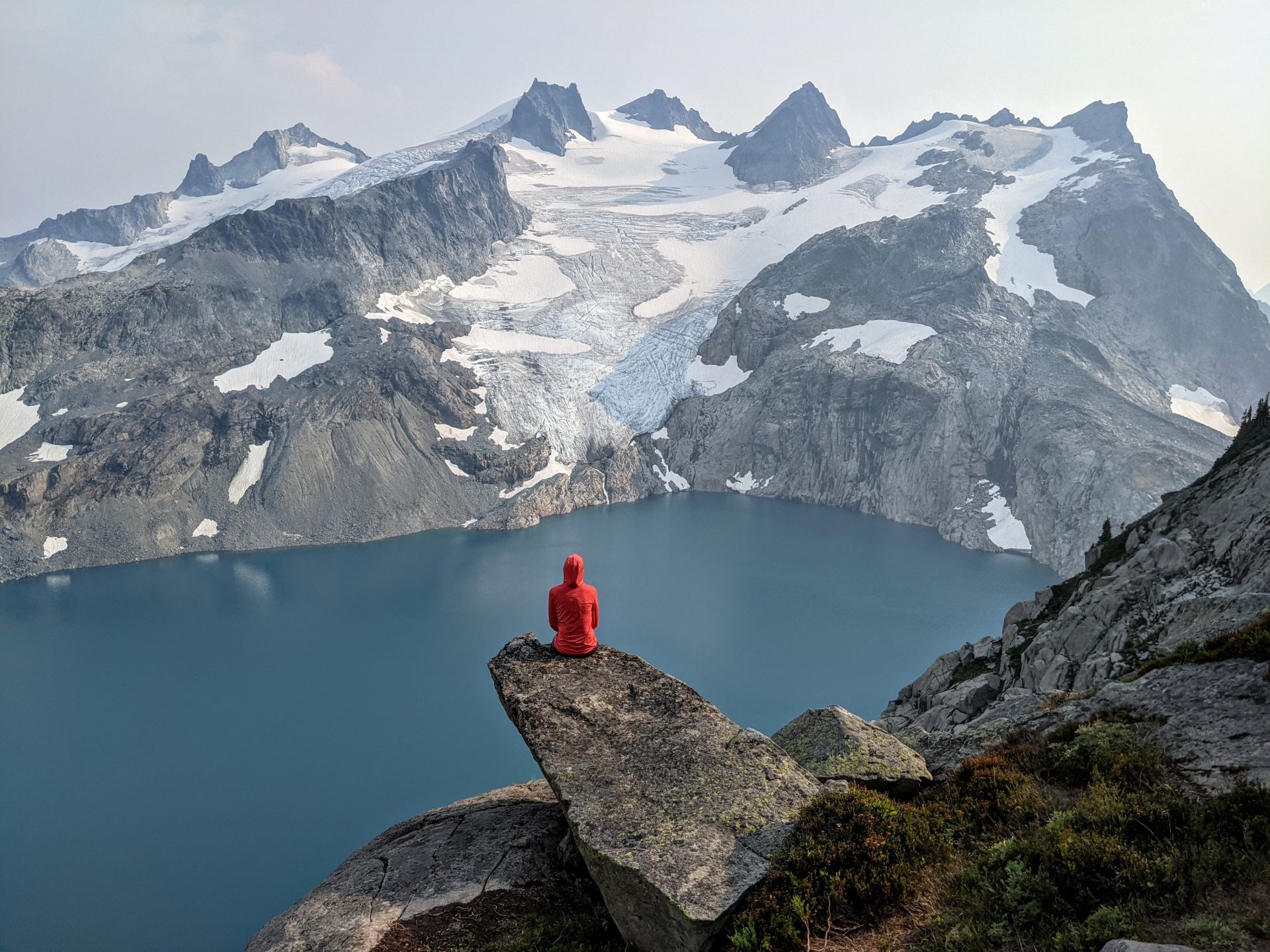 A person sitting on a rock ledge high above Pea Soup Lake in Alpine Lakes Wilderness