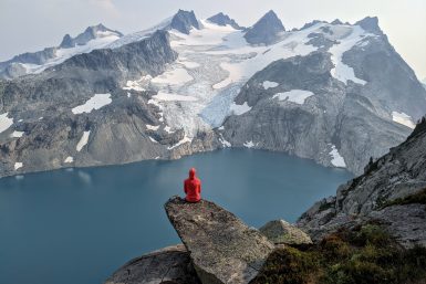 A person sitting on a rock ledge high above Pea Soup Lake in Alpine Lakes Wilderness
