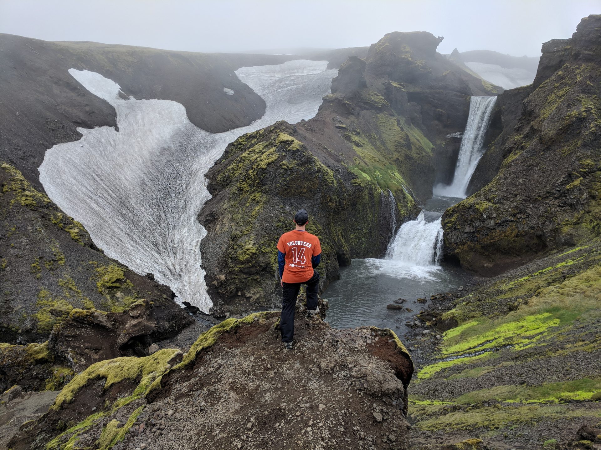 A hiker overlooking a tiered waterfall along the Fimmvorduhals trail in Iceland