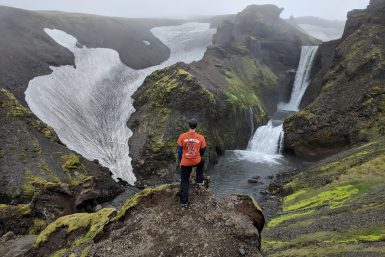 A hiker overlooking a tiered waterfall along the Fimmvorduhals trail in Iceland