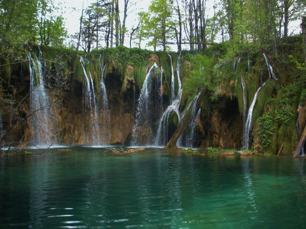 Four separate waterfalls flowing into a green pool of water at Plitvice Lakes National Park