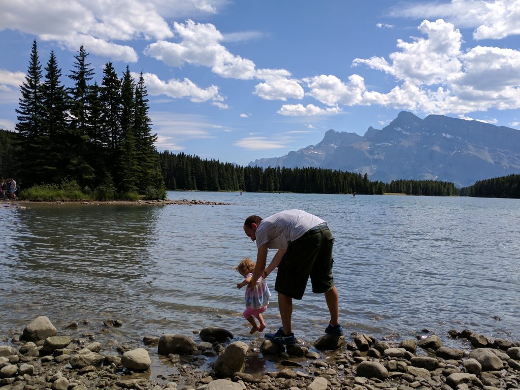 A man dipping the toes of a small child in the water at Two Jack Lake