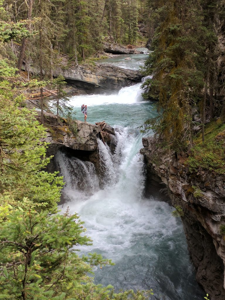 A hiker standing near cascading water at Johnston Canyon