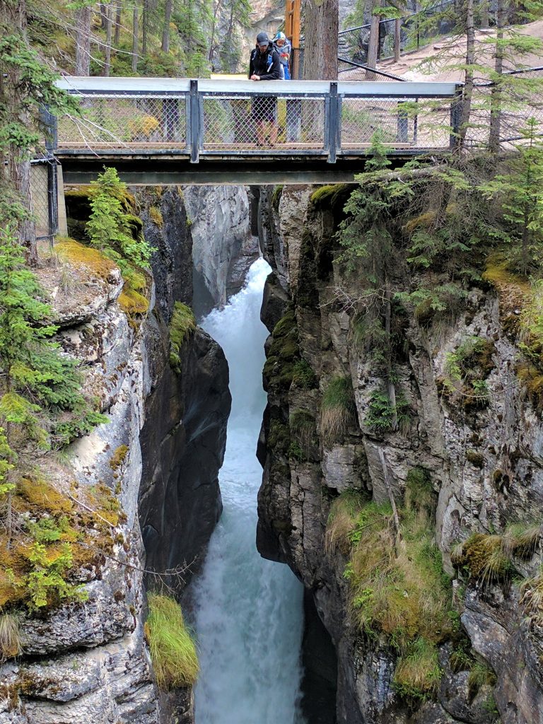 A hiker and young child looking down at Maligne Canyon from a bridge over the water