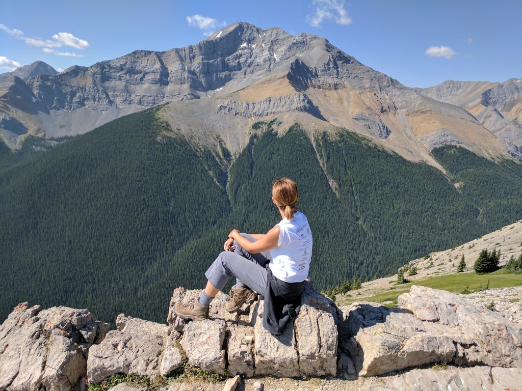 A woman sitting on a rock looking out at a massive mountain in the Canadian Rockies