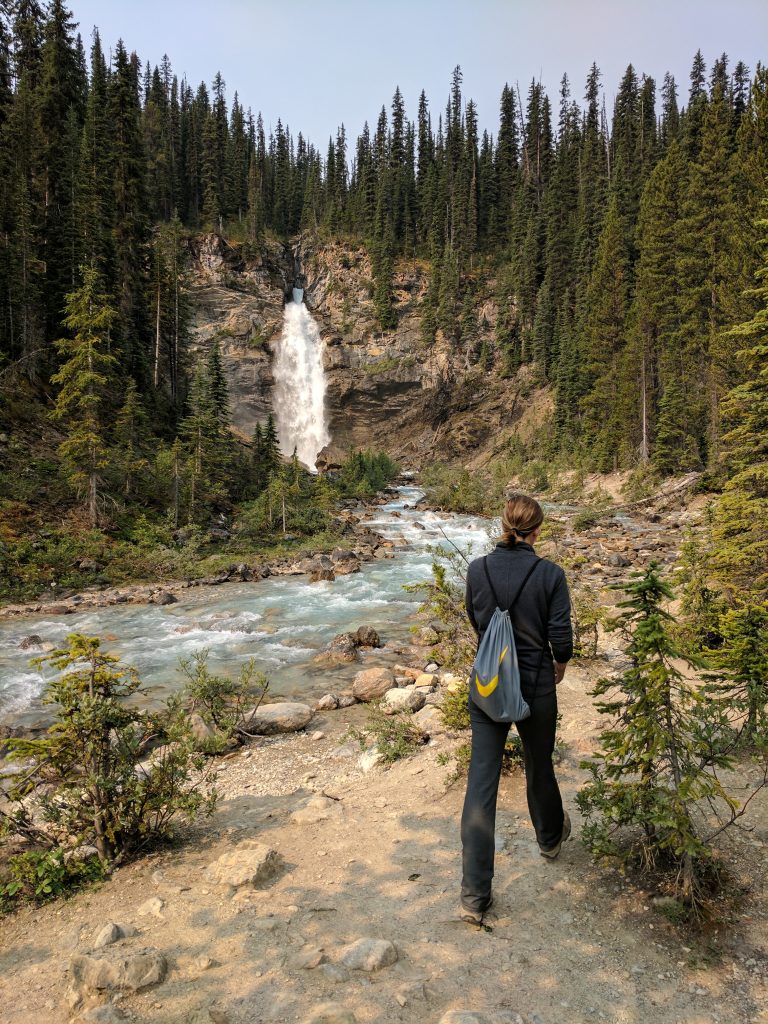 A hiker walking past a stream with Laughing Falls in the background