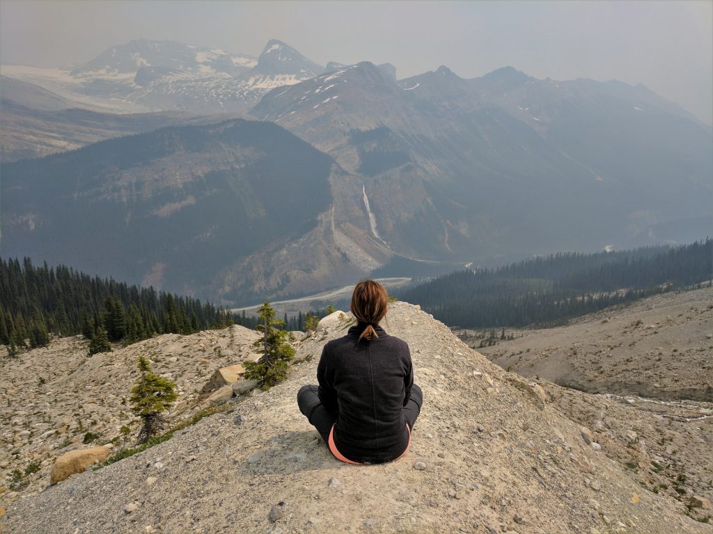 A woman sitting down overlooking Takakkaw Falls on a smoky day