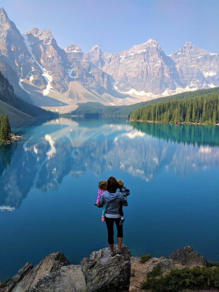 A woman holding children standing in front of mountains reflected in Moraine Lake