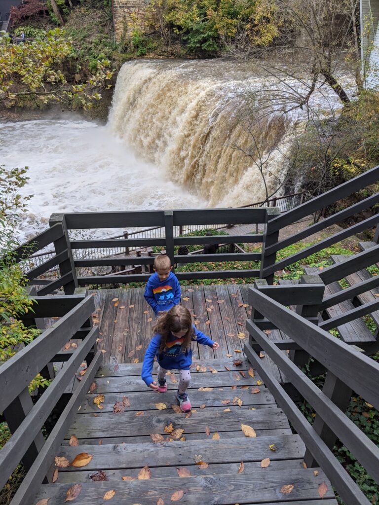 2 young children climbing wooden stairs with Chagrin Falls in the background