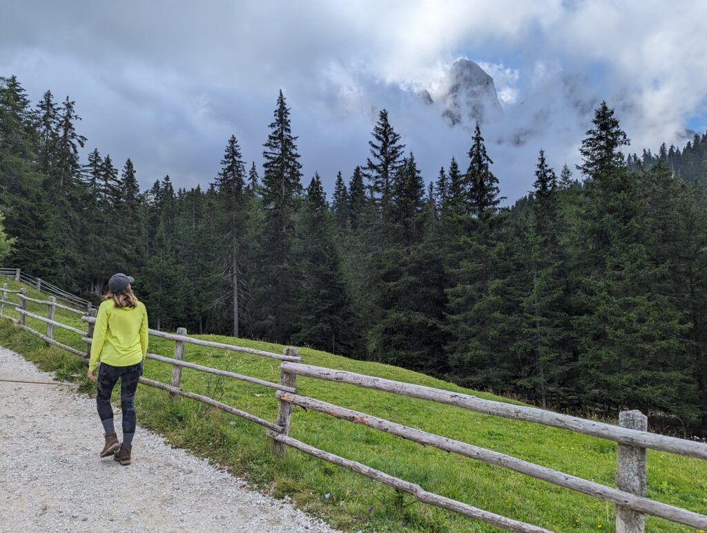 A hiker looking at a mountain peaking through the clouds in Puez Odle Nature Park, Dolomites