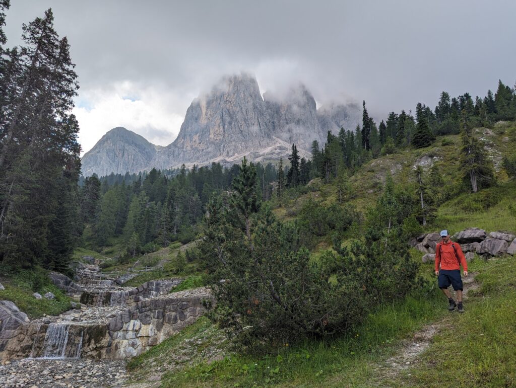 A hiker near a waterfall with mountains in Puez Odle Nature Park, Dolomites