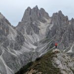 A hiker standing on a point looking at the jagged mountains of Cadini di Misurina