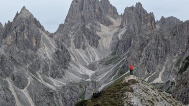 A hiker standing on a point looking at the jagged mountains of Cadini di Misurina