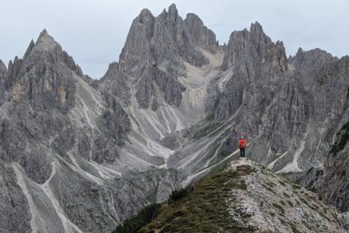 A hiker standing on a point looking at the jagged mountains of Cadini di Misurina