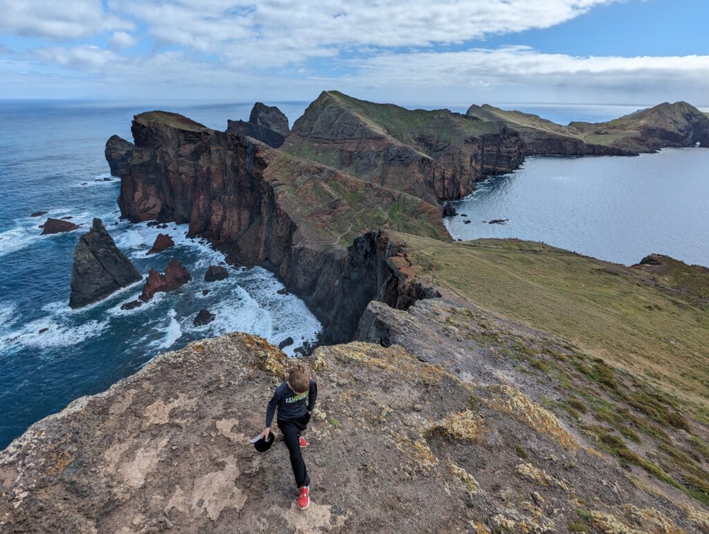 A young boy walking towards the vantage point of a narrow, rugged peninsula surrounded by water on Madeira