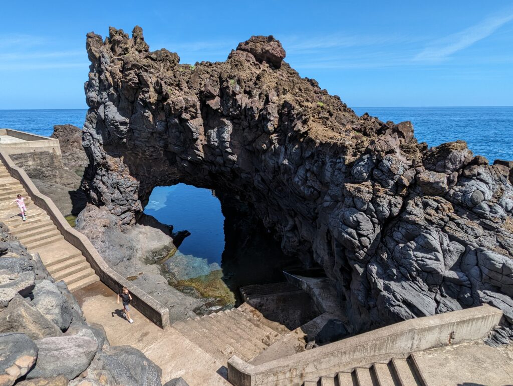 Kids going down stairs leading to a rock arch over water in Seixal, Madeira