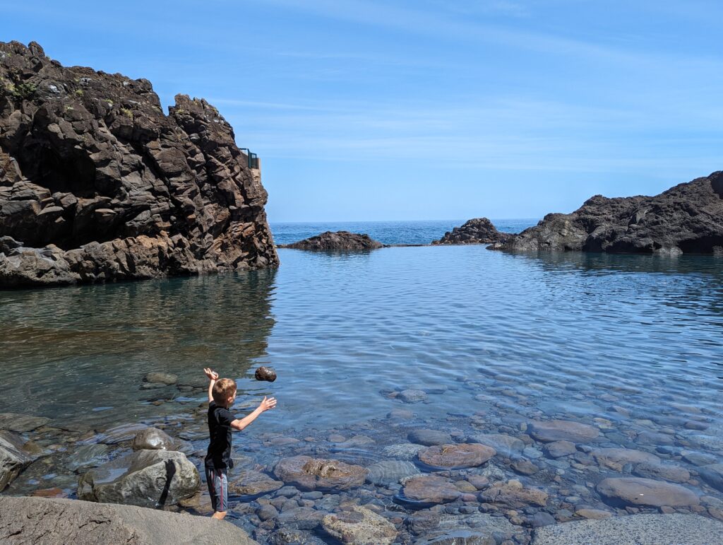 A boy throwing a rock into a pool of water on Madeira