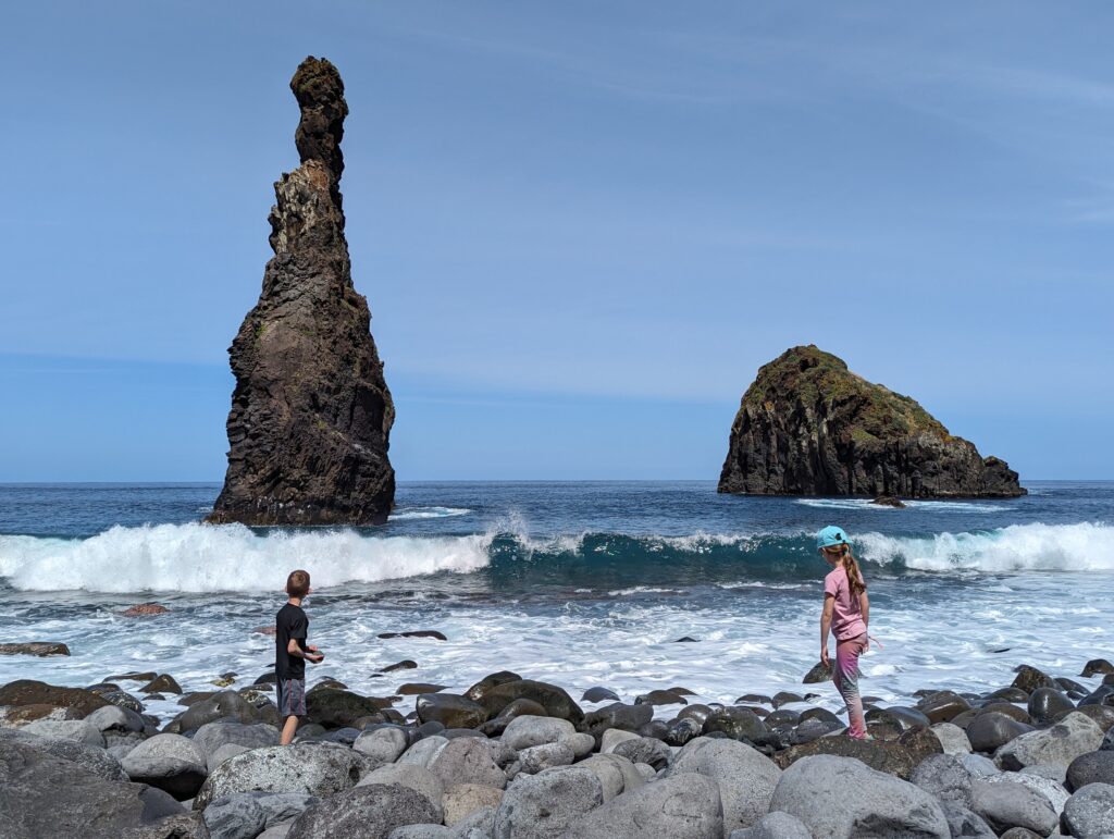 Two kids on a rocky beach with sea stacks in the background in Madeira
