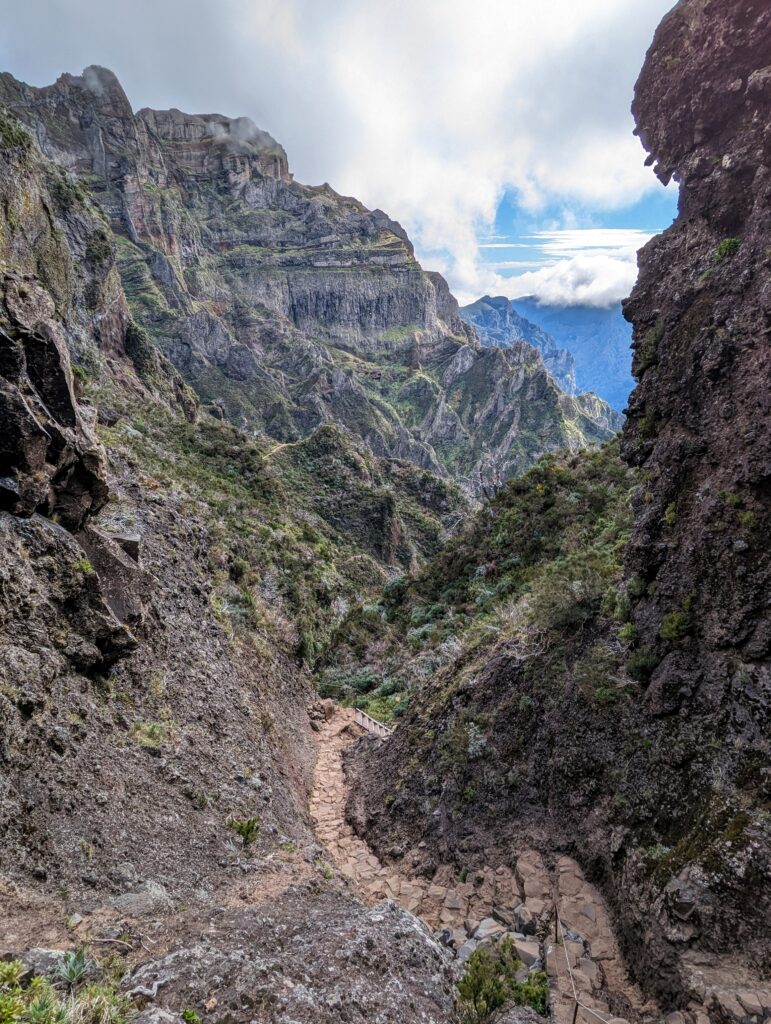 A path winding down and through green and rocky mountains on a cloudy day on Madeira