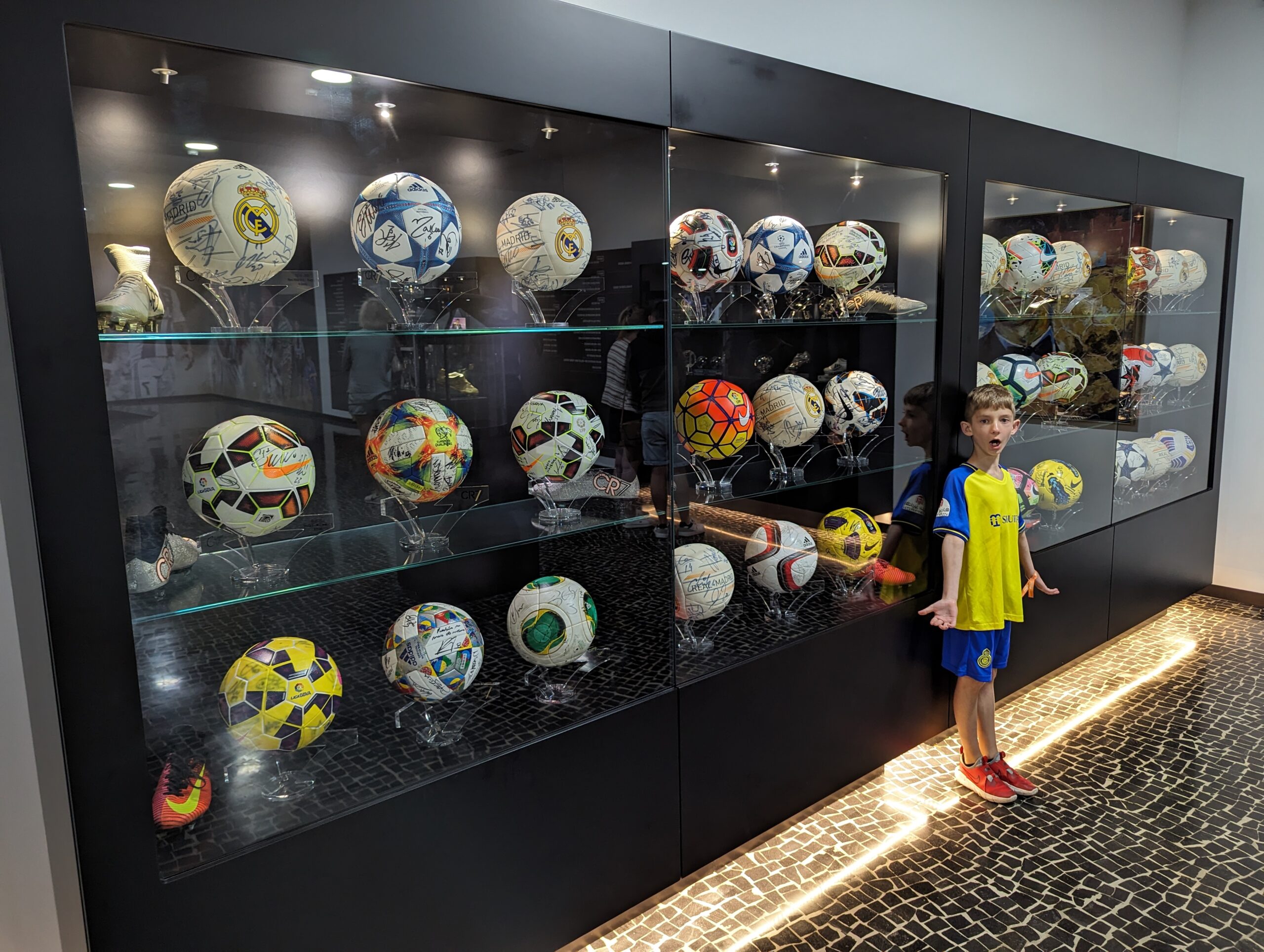 A boy standing in front of a display case of soccer balls at the CR7 museum on Madeira