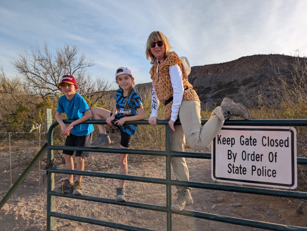 An adult and two children atop a metal gate near Las Cruces