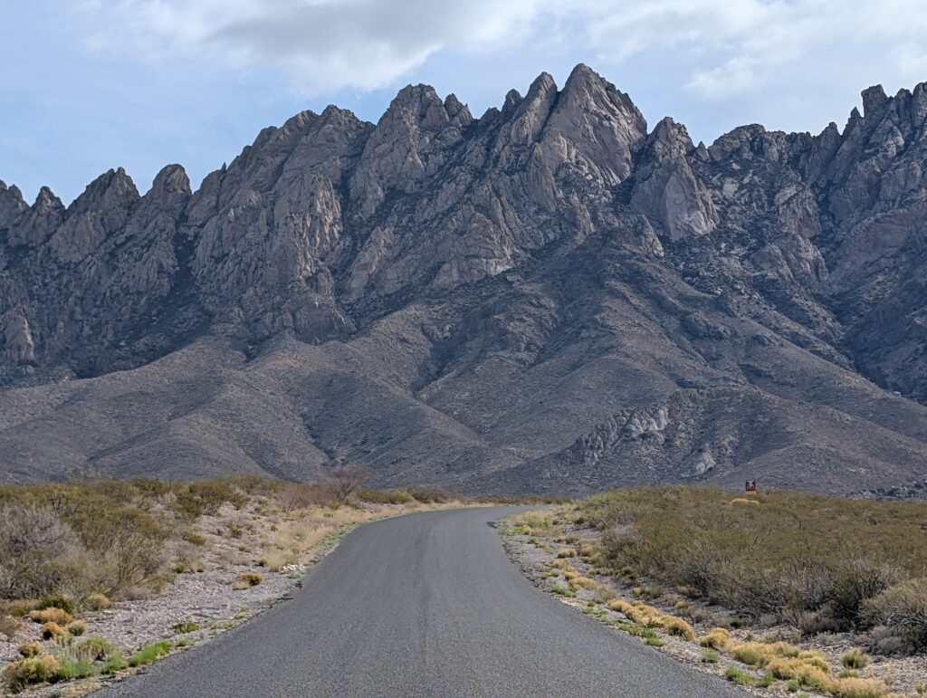 A paved road leading to large, jagged mountains