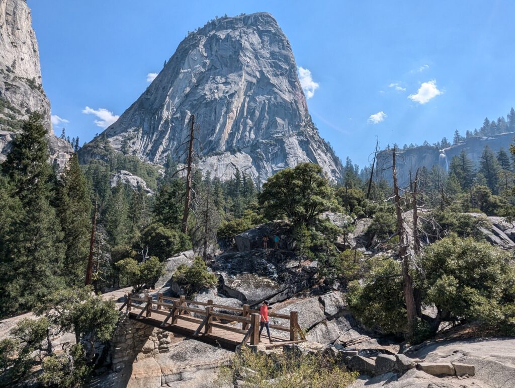 A woman walking across a wooden bridge with a large rock formation behind her in Yosemite National Park