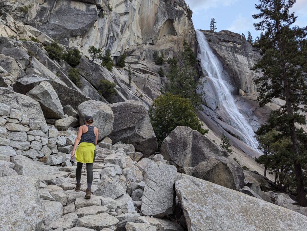 A woman hiking on a stone path with a waterfall on the right side