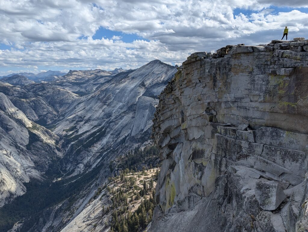 A hiker atop a large, flat rock section overlooking a rock valley below