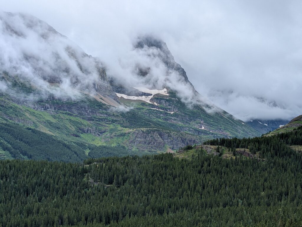 Clouds mostly covering mountain peaks with a clear green valley below