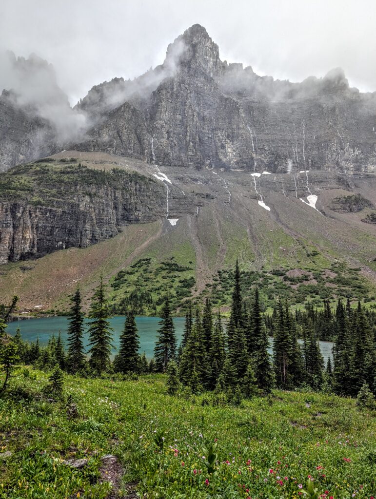 A cloud-covered mountain scene with several small waterfalls and trees in the foreground