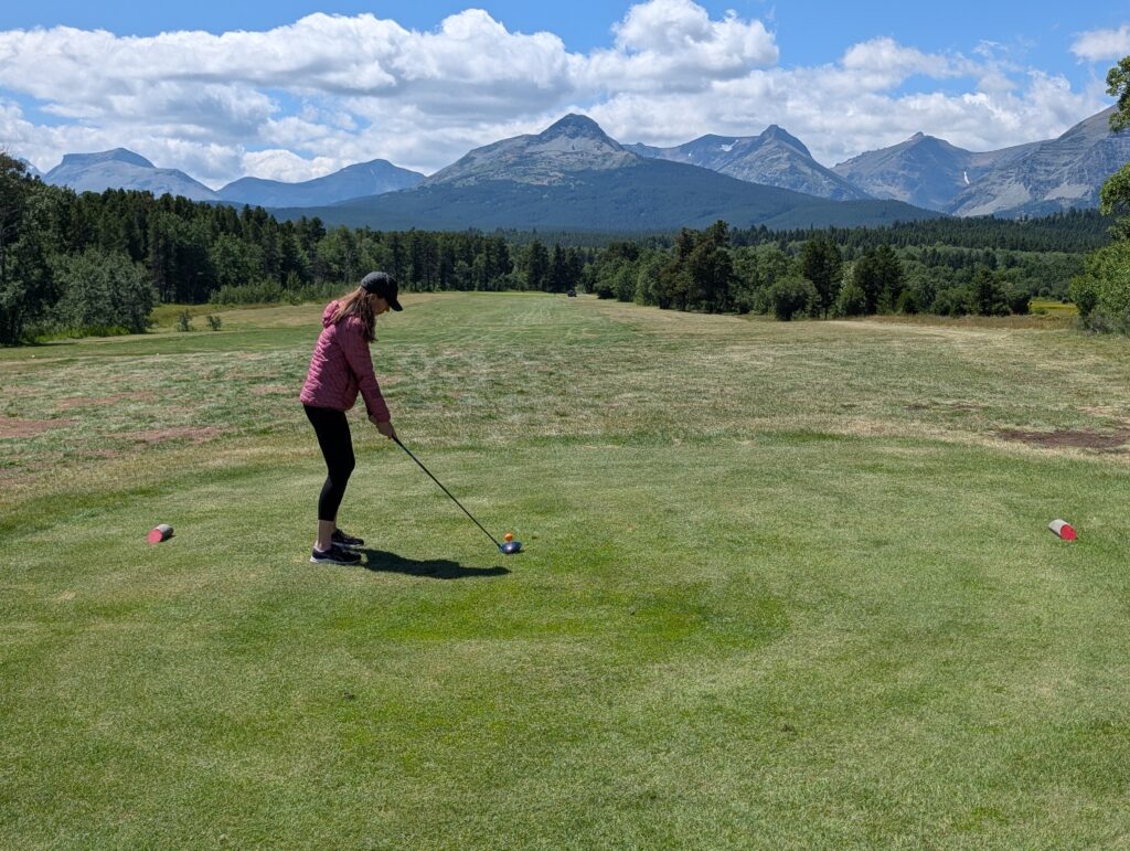 A woman golfer ready to hit a tee shot with mountains in the background