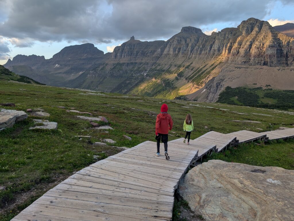 Two young kids walking on a boardwalk with a long mountain wall far away