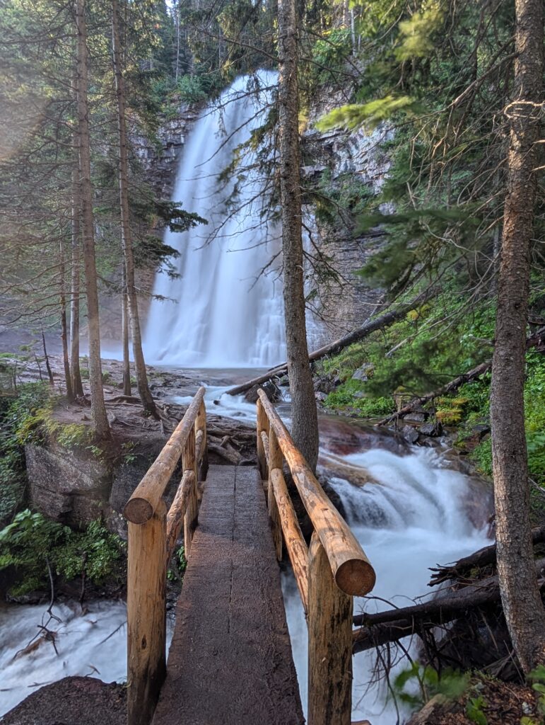 An empty wood bridge leading to Virginia Falls which is partially covered by trees in Glacier National Park