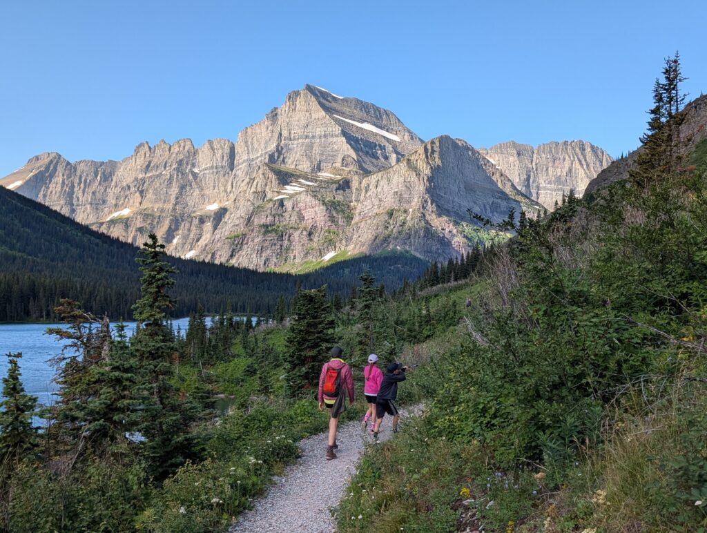 Three hikers walking on a stone path with mountains in the background in the Many Glacier area