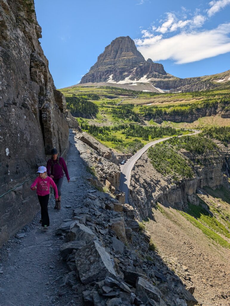A mother and daughter walking on a narrow path with a high cliff on one side and dropoff on the other