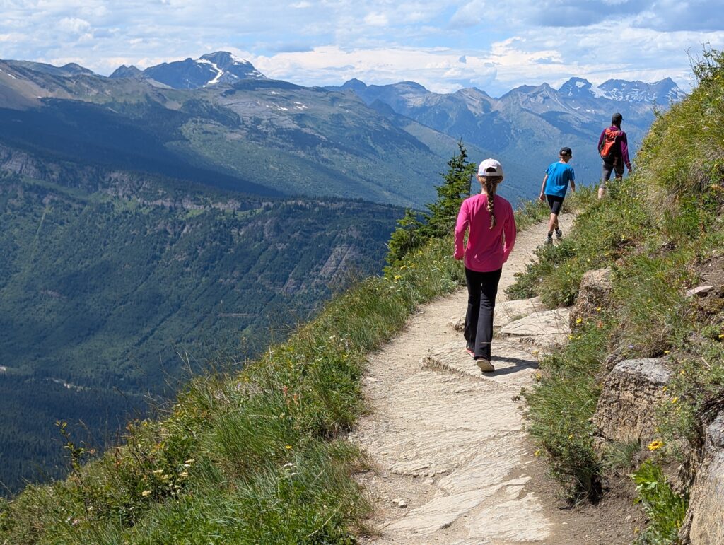 3 hikers along a dirt path on the edge of a long dropoff in the mountains