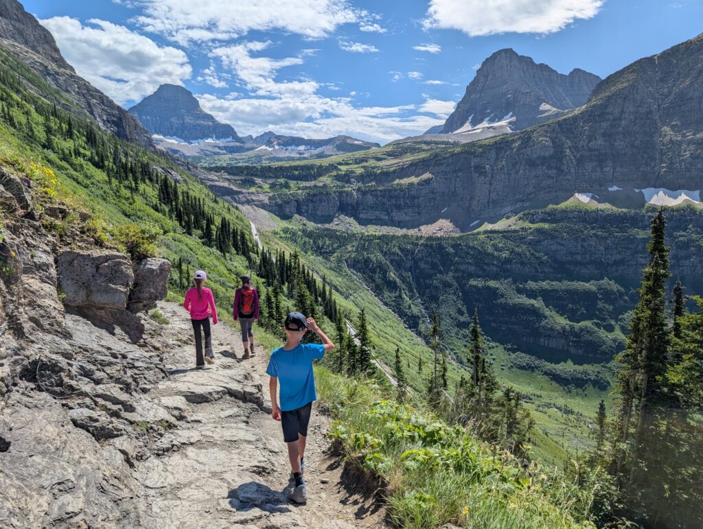 Three hikers with two mountain peaks and a valley near Logan Pass