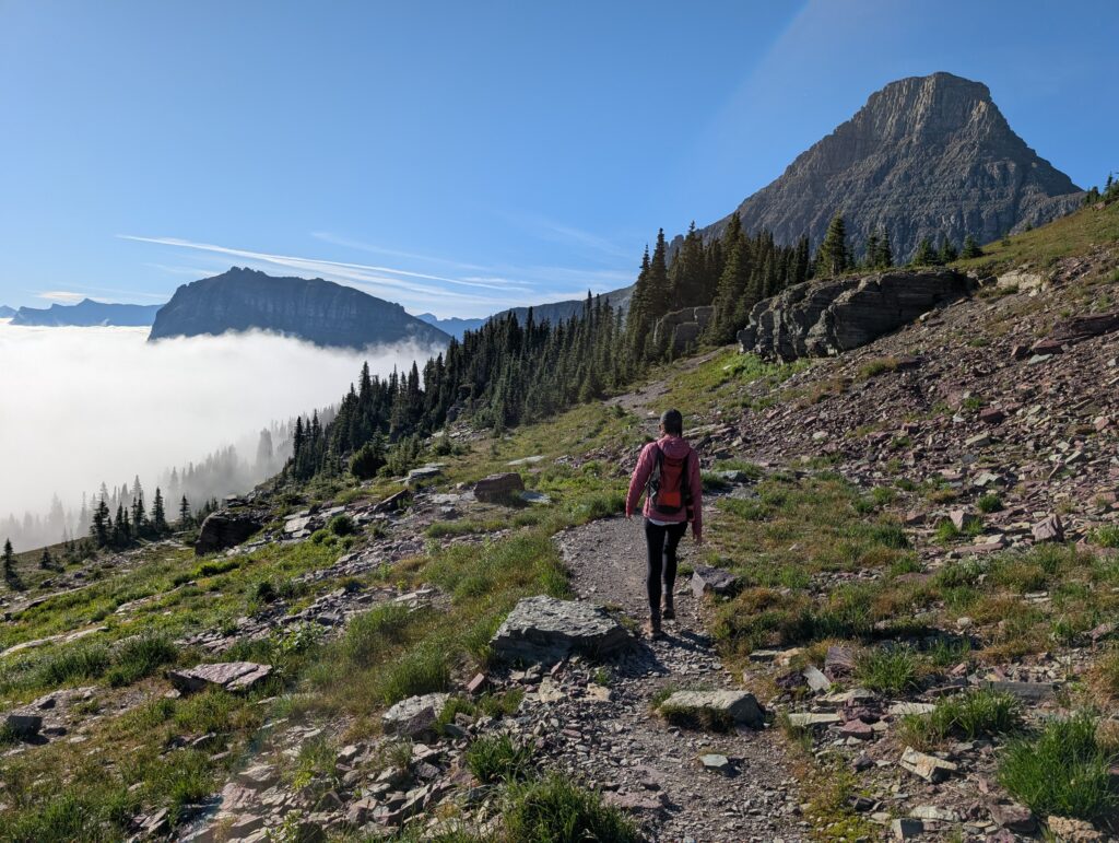 A hiker walking along a path above clouds with a mountain peaking out