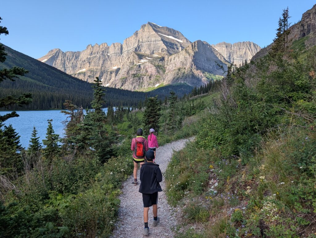 Three hikers walking along a stone path with a small body of water and mountains in front of them