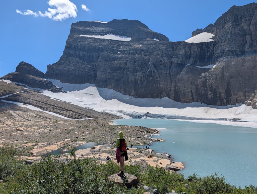 A person standing on a rock in front of a glacier-filled body of water with mountains