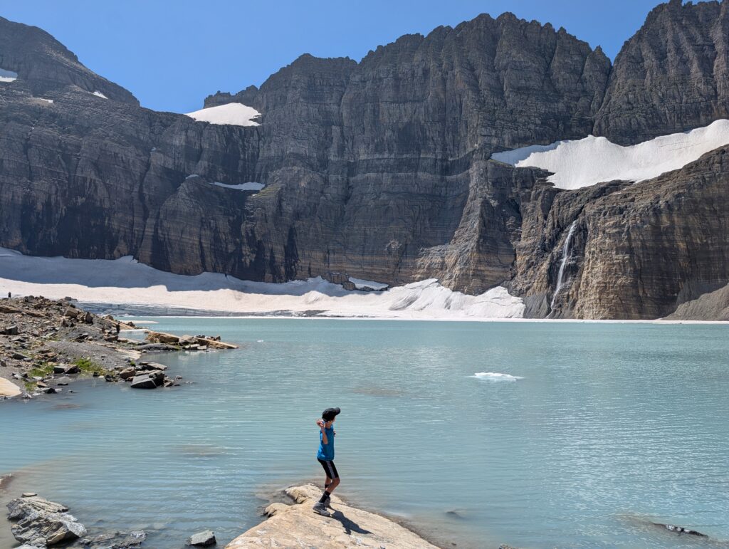 A young boy just about to throw a rock into an alpine lake with snow and mountains