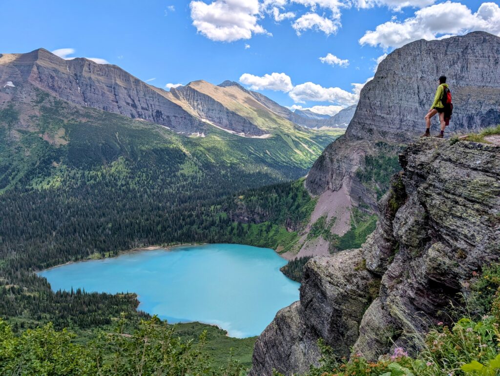 A hiker standing on a ledge high above a blue lake
