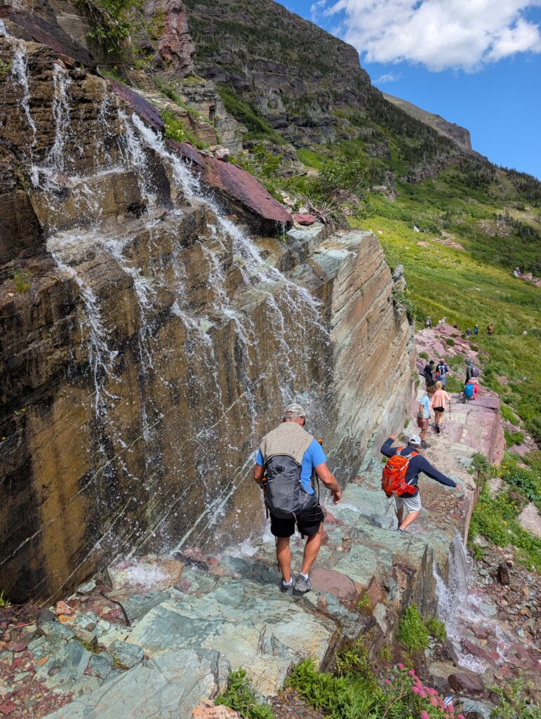 Hikers carefully descending a stone staircase with water falling down onto the path