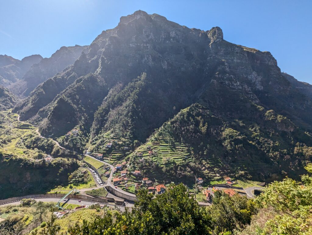 A rugged green mountain with buildings and a road at the foot of it