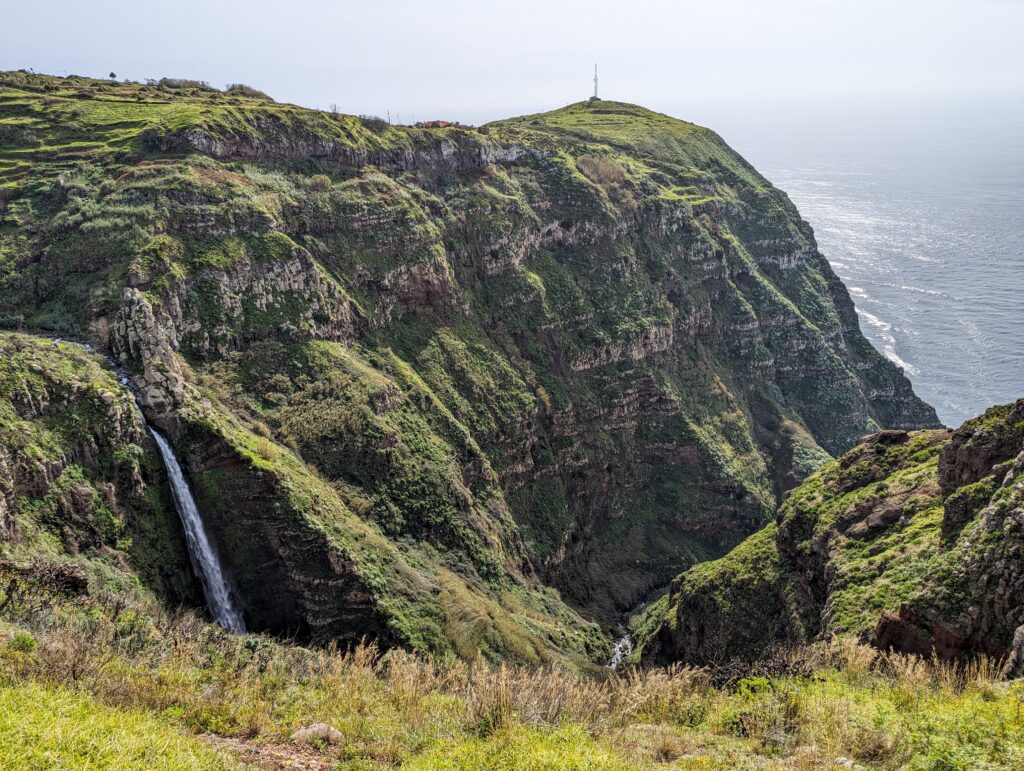 A rugged green canyon leading to sea with the start of a waterfall on the side of it
