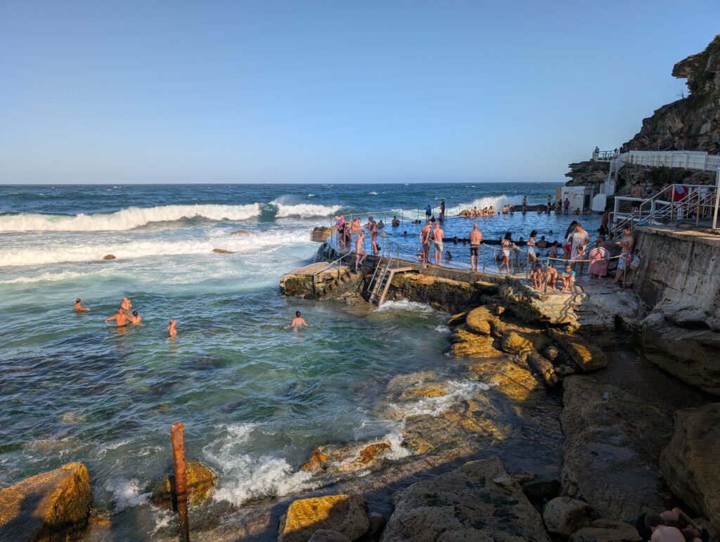 People in and around a pool of water right next to the ocean