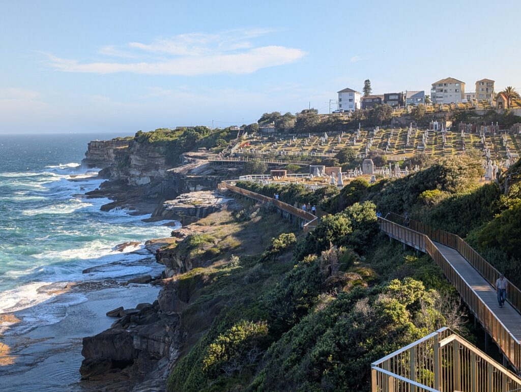A boardwalk leads along a rocky coast to a cemetery by the water