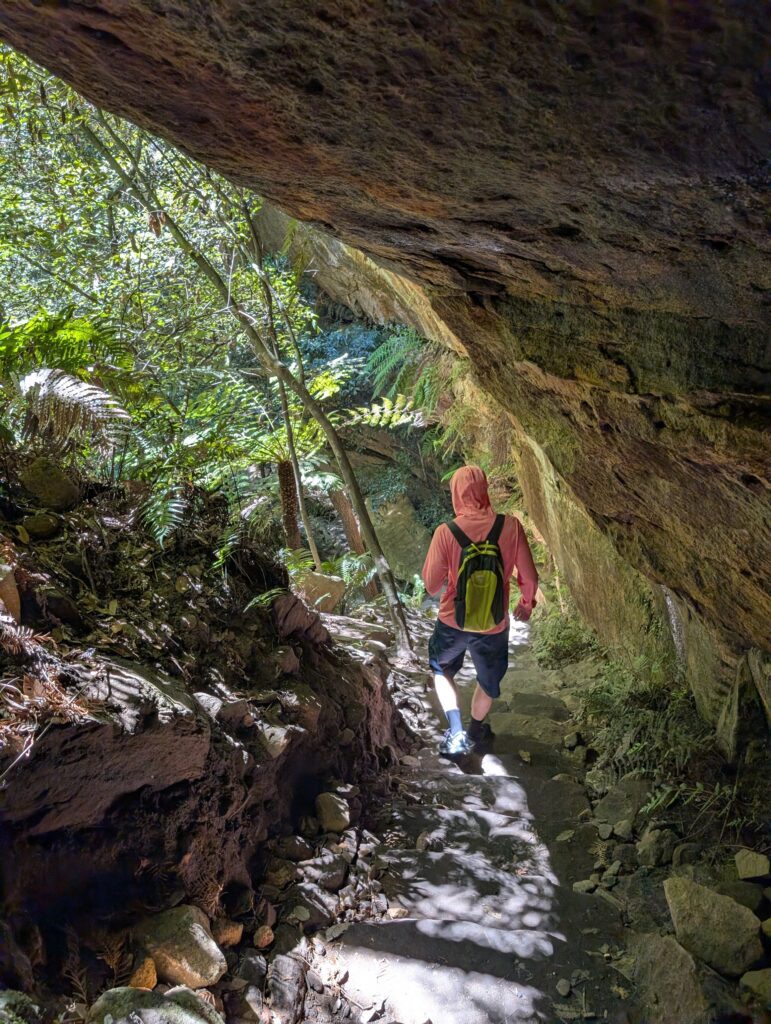 A man walking under a large overhanging rock