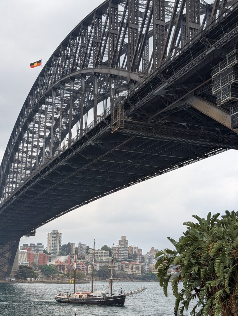 A wooden ship passing beneath the Sydney Harbour Bridge